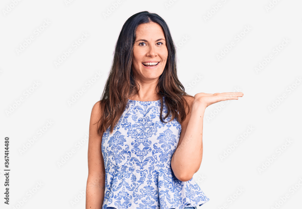 Young beautiful brunette woman wearing casual t-shirt smiling cheerful presenting and pointing with palm of hand looking at the camera. Young beautiful brunette woman wearing casual t-shirt smiling cheerful presenting and pointing with palm of hand looking at the camera.