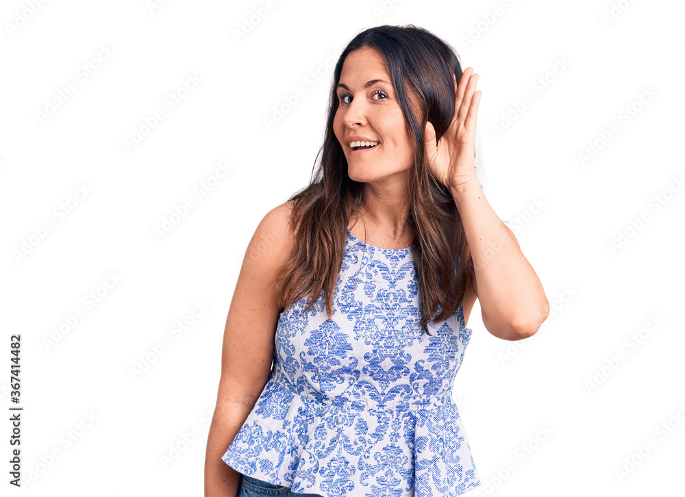 Young beautiful brunette woman wearing casual t-shirt smiling with hand over ear listening an hearing to rumor or gossip. deafness concept.