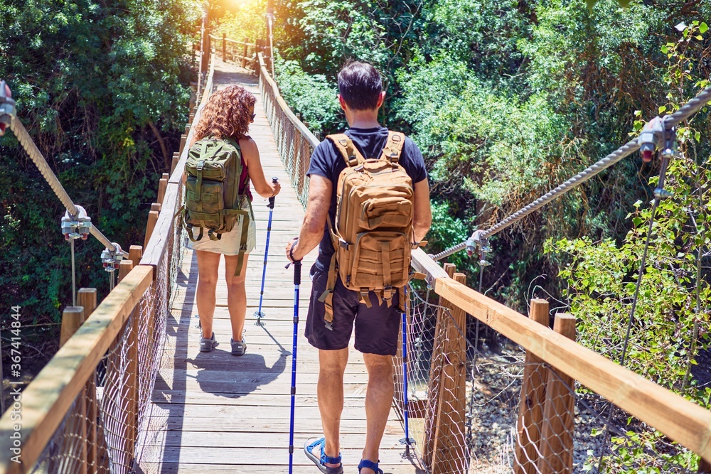 Beautiful couple of hiker wearing explorer clothes and  backpack. Walking on back view at runway over forest landscape background.