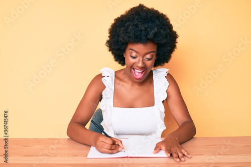 Young african american woman writing book celebrating victory with happy smile and winner expression with raised hands