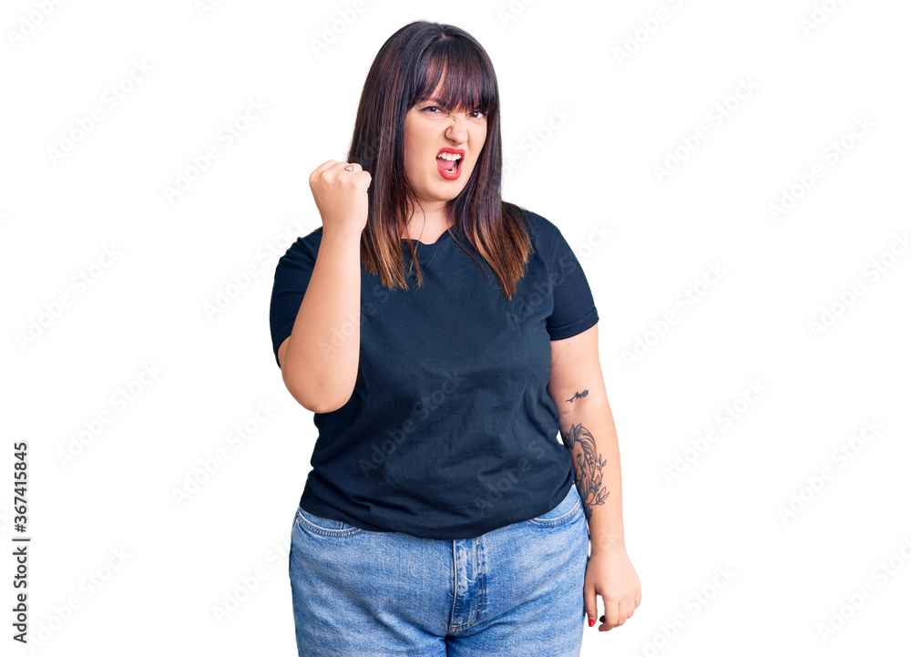 Young plus size woman wearing casual clothes angry and mad raising fist frustrated and furious while shouting with anger. rage and aggressive concept. Young plus size woman wearing casual clothes angry and mad raising fist frustrated and furious while shouting with anger. rage and aggressive concept.