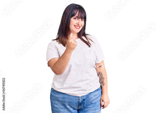 Young plus size woman wearing casual clothes beckoning come here gesture with hand inviting welcoming happy and smiling