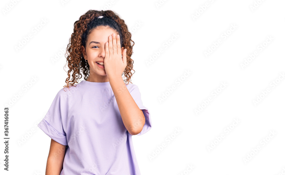 Beautiful kid girl with curly hair wearing casual clothes covering one eye with hand, confident smile on face and surprise emotion. Beautiful kid girl with curly hair wearing casual clothes covering one eye with hand, confident smile on face and surprise emotion.
