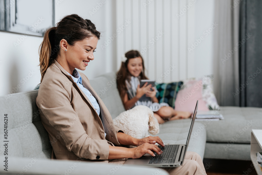 Beautiful young mother working from home while her daughter watching online school class. Social distancing and Covid-19 or Coronavirus lifestyle.