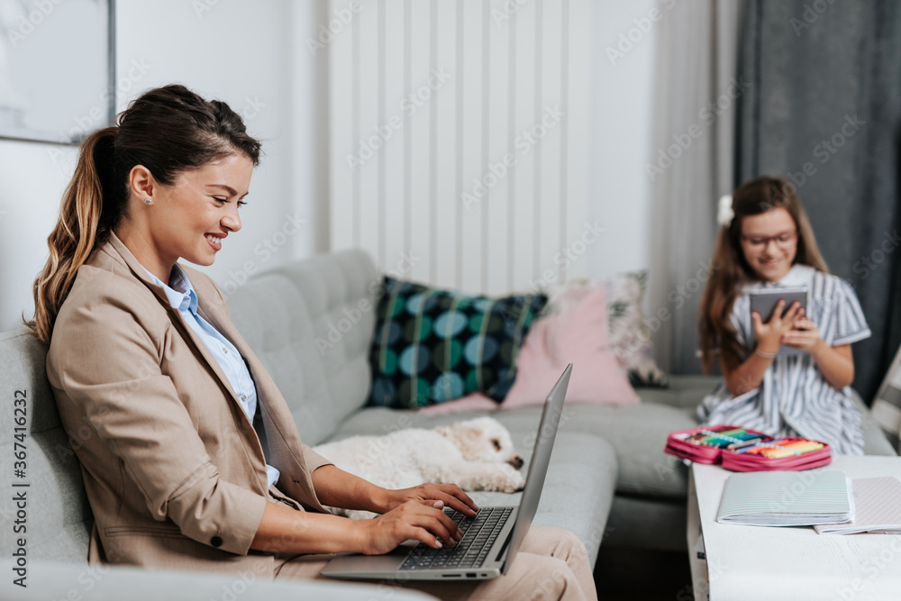 Beautiful young mother working from home while her daughter watching online school class. Social distancing and Covid-19 or Coronavirus lifestyle. Beautiful young mother working from home while her daughter watching online school class. Social distancing and Covid-19 or Coronavirus lifestyle.