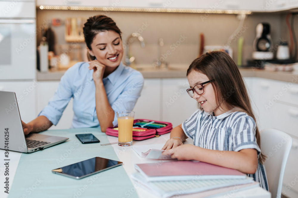 Beautiful young mother helping her younger daughter with homework.