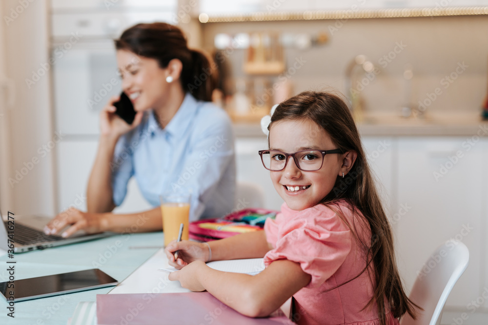Beautiful young mother working from home while her daughter watching online school class. Social distancing and Covid-19 or Coronavirus lifestyle. Beautiful young mother working from home while her daughter watching online school class. Social distancing and Covid-19 or Coronavirus lifestyle.