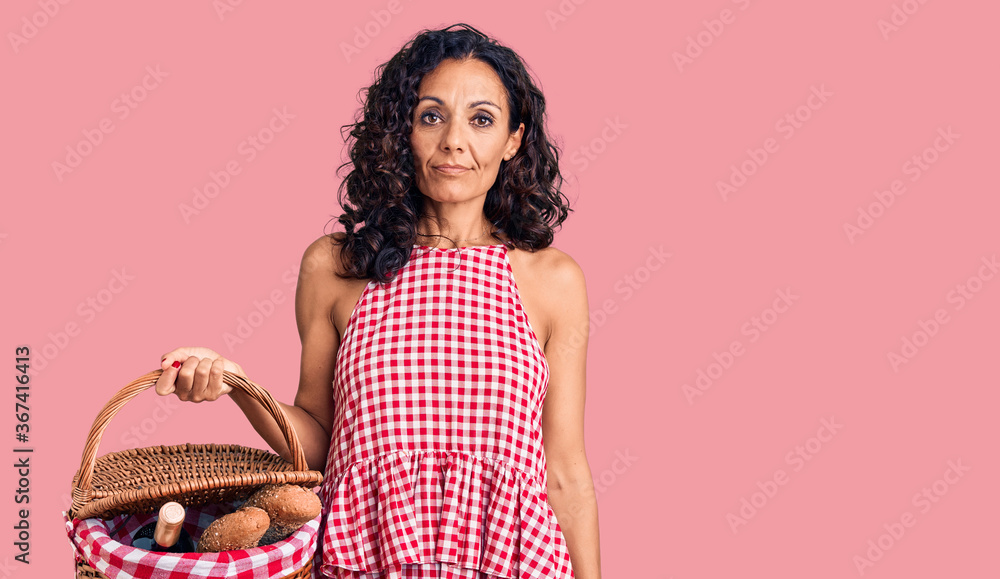 Middle age beautiful woman holding picnic basket with food thinking attitude and sober expression looking self confident Middle age beautiful woman holding picnic basket with food thinking attitude and sober expression looking self confident