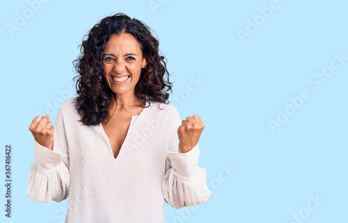 Middle age beautiful woman wearing casual sweater very happy and excited doing winner gesture with arms raised, smiling and screaming for success. celebration concept.