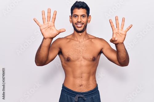 Young latin man standing shirtless showing and pointing up with fingers number nine while smiling confident and happy. © Krakenimages.com
