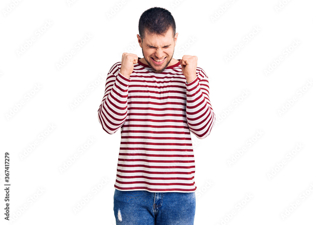 Young handsome man wearing striped sweater excited for success with arms raised and eyes closed celebrating victory smiling. winner concept. Young handsome man wearing striped sweater excited for success with arms raised and eyes closed celebrating victory smiling. winner concept.