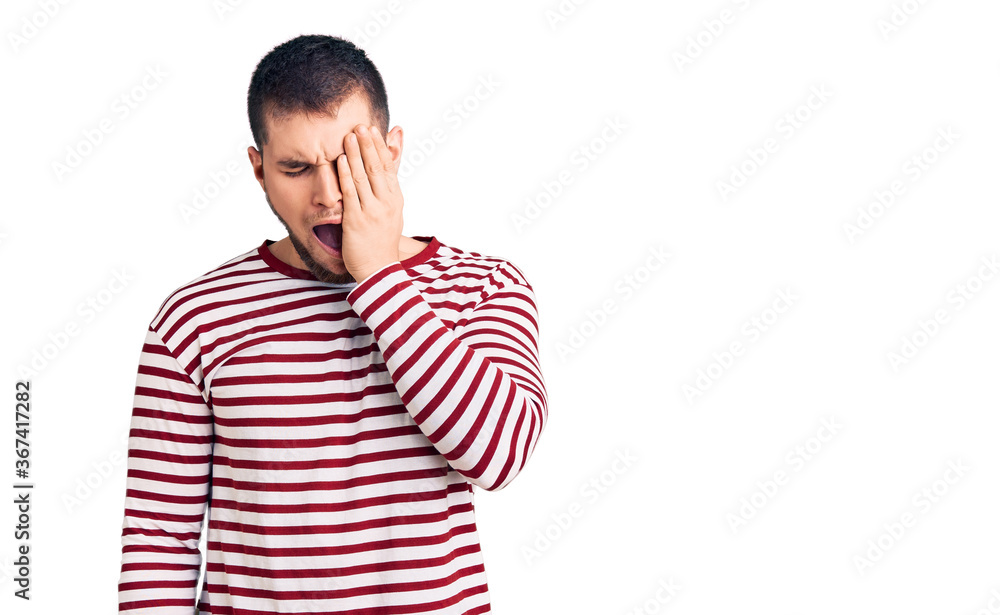 Young handsome man wearing striped sweater yawning tired covering half face, eye and mouth with hand. face hurts in pain. Young handsome man wearing striped sweater yawning tired covering half face, eye and mouth with hand. face hurts in pain.