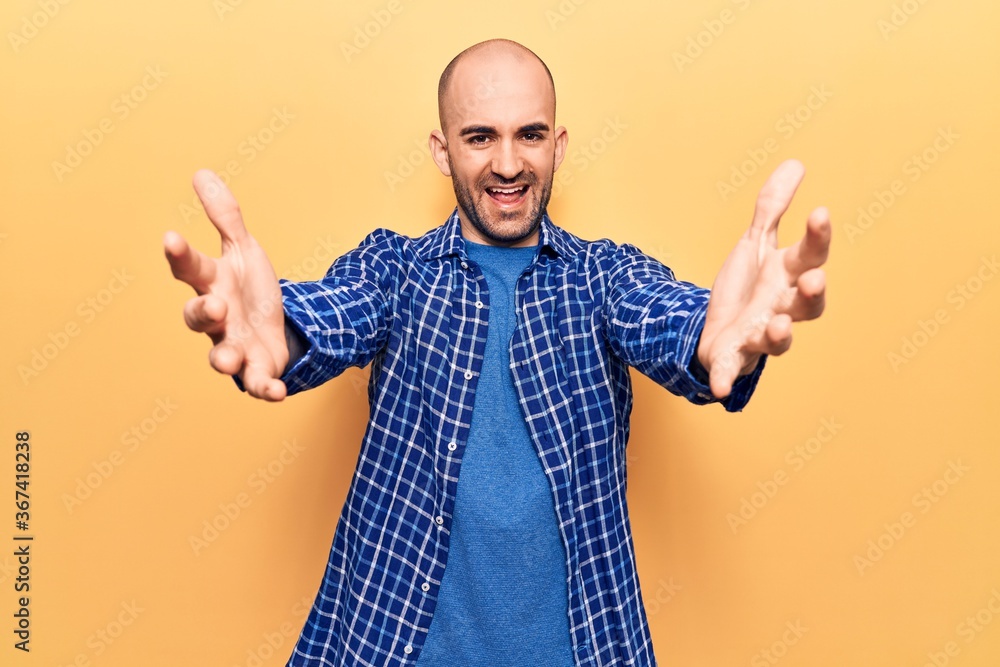 Young handsome bald man wearing casual shirt looking at the camera smiling with open arms for hug. cheerful expression embracing happiness. Young handsome bald man wearing casual shirt looking at the camera smiling with open arms for hug. cheerful expression embracing happiness.