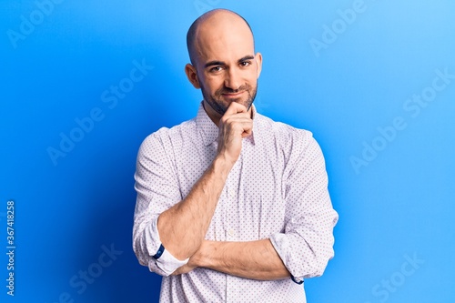 Young handsome bald man wearing elegant shirt smiling looking confident at the camera with crossed arms and hand on chin. thinking positive.