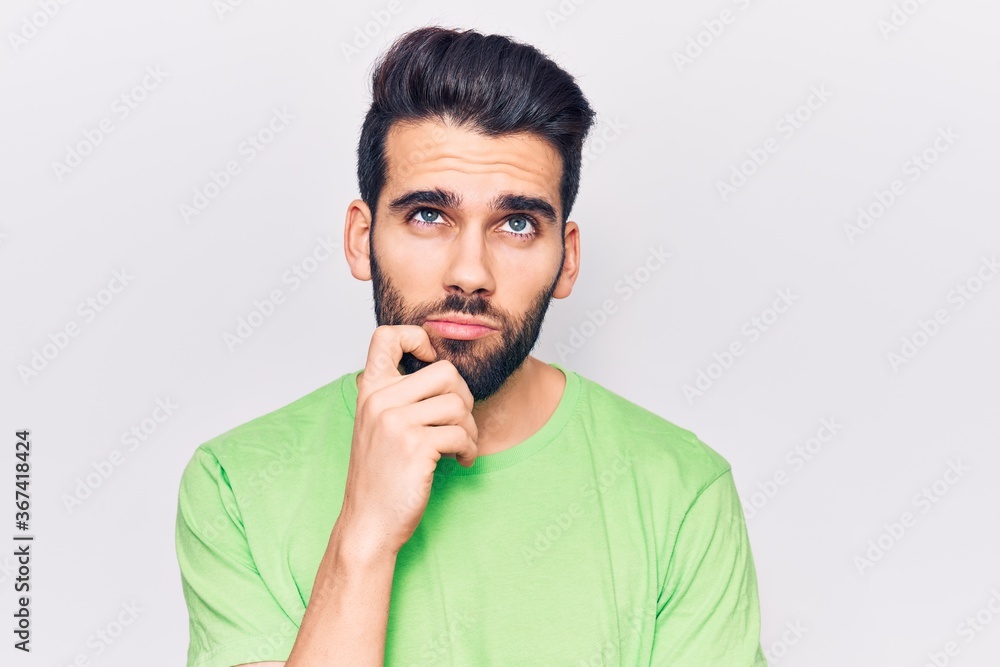 Young handsome man with beard wearing casual t-shirt serious face thinking about question with hand on chin, thoughtful about confusing idea Young handsome man with beard wearing casual t-shirt serious face thinking about question with hand on chin, thoughtful about confusing idea