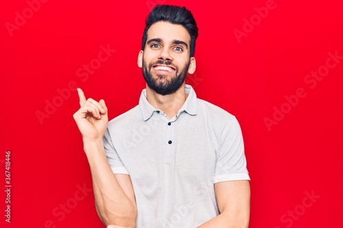 Young handsome man with beard wearing casual polo with a big smile on face, pointing with hand and finger to the side looking at the camera. © Krakenimages.com