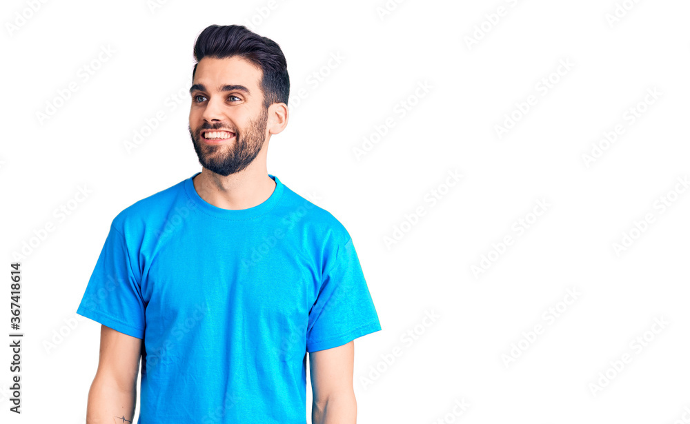 Young handsome man with beard wearing casual t-shirt looking away to side with smile on face, natural expression. laughing confident. Young handsome man with beard wearing casual t-shirt looking away to side with smile on face, natural expression. laughing confident.
