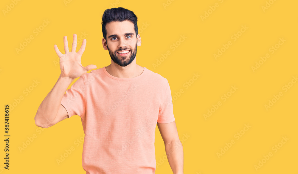 Young handsome man with beard wearing casual t-shirt showing and pointing up with fingers number five while smiling confident and happy. Young handsome man with beard wearing casual t-shirt showing and pointing up with fingers number five while smiling confident and happy.
