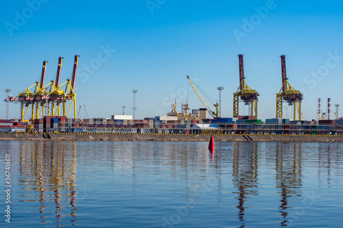Seaport. Water, port cranes and containers under a blue sky. Cargo transportation by water. Merchant fleet. Panorama of the port on a Sunny day.