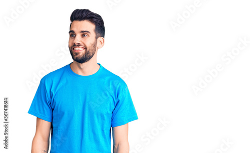 Young handsome man with beard wearing casual t-shirt looking away to side with smile on face, natural expression. laughing confident. © Krakenimages.com