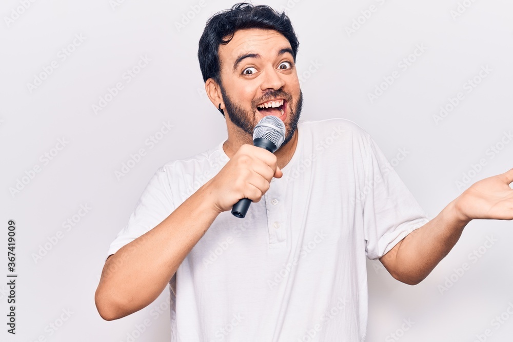 Young hispanic man singing song using microphone celebrating achievement with happy smile and winner expression with raised hand