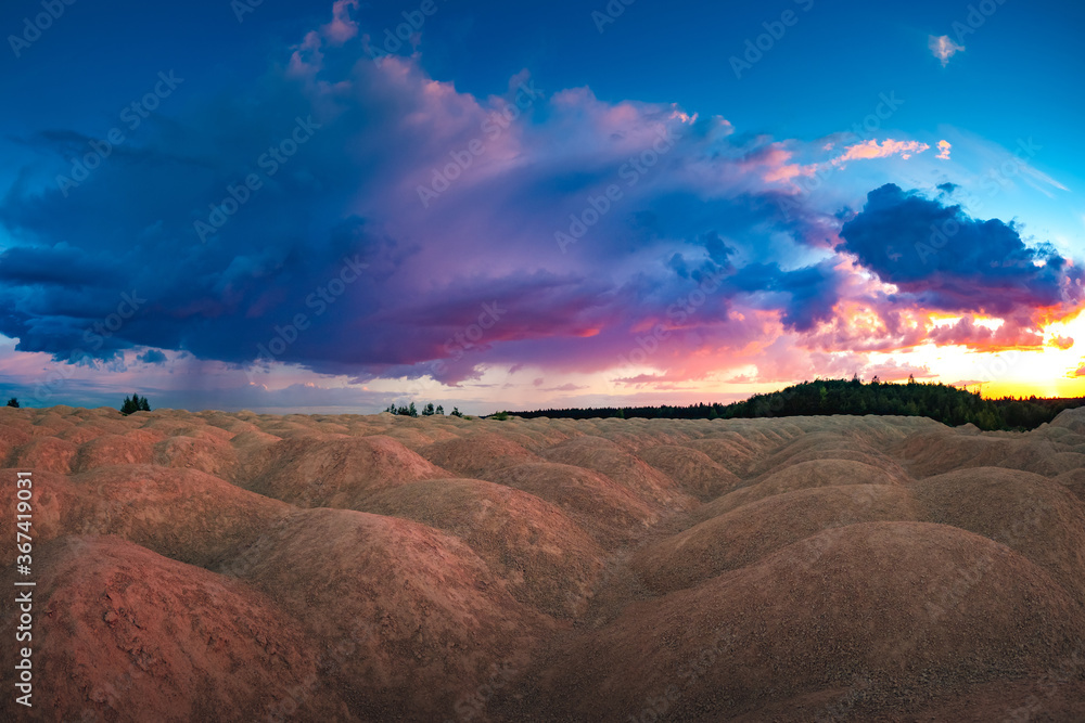 An unusual natural landscape. The landscape is similar to the planet Mars. Sand hills on the background of the colorful sky. Sand, trees, and clouds. An unusual natural landscape. The landscape is similar to the planet Mars. Sand hills on the background of the colorful sky. Sand, trees, and clouds.