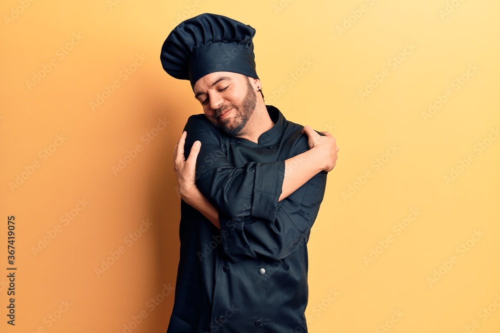 Young hispanic man wearing cooker uniform hugging oneself happy and positive, smiling confident. self love and self care Young hispanic man wearing cooker uniform hugging oneself happy and positive, smiling confident. self love and self care