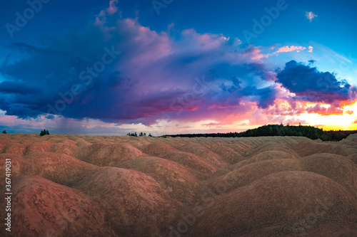 An unusual natural landscape. The landscape is similar to the planet Mars. Sand hills on the background of the colorful sky. Sand, trees, and clouds.