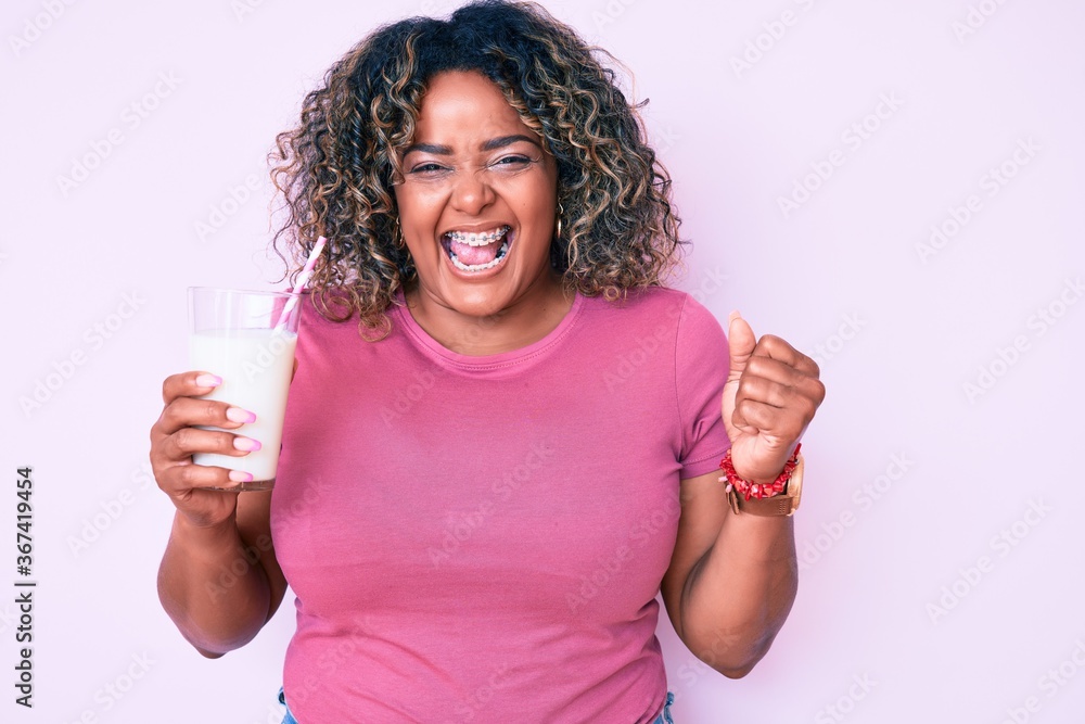 Young african american plus size woman drinking glass of milk screaming proud, celebrating victory and success very excited with raised arms Young african american plus size woman drinking glass of milk screaming proud, celebrating victory and success very excited with raised arms