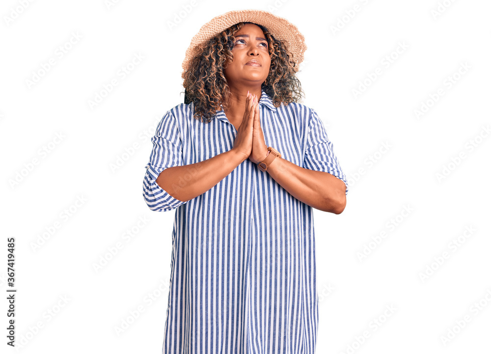 Young african american plus size woman wearing summer hat begging and praying with hands together with hope expression on face very emotional and worried. begging. Young african american plus size woman wearing summer hat begging and praying with hands together with hope expression on face very emotional and worried. begging.