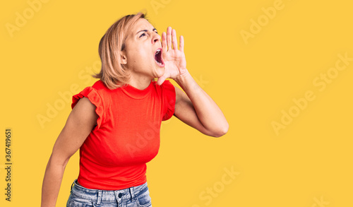 Young blonde woman wearing casual clothes shouting and screaming loud to side with hand on mouth. communication concept.