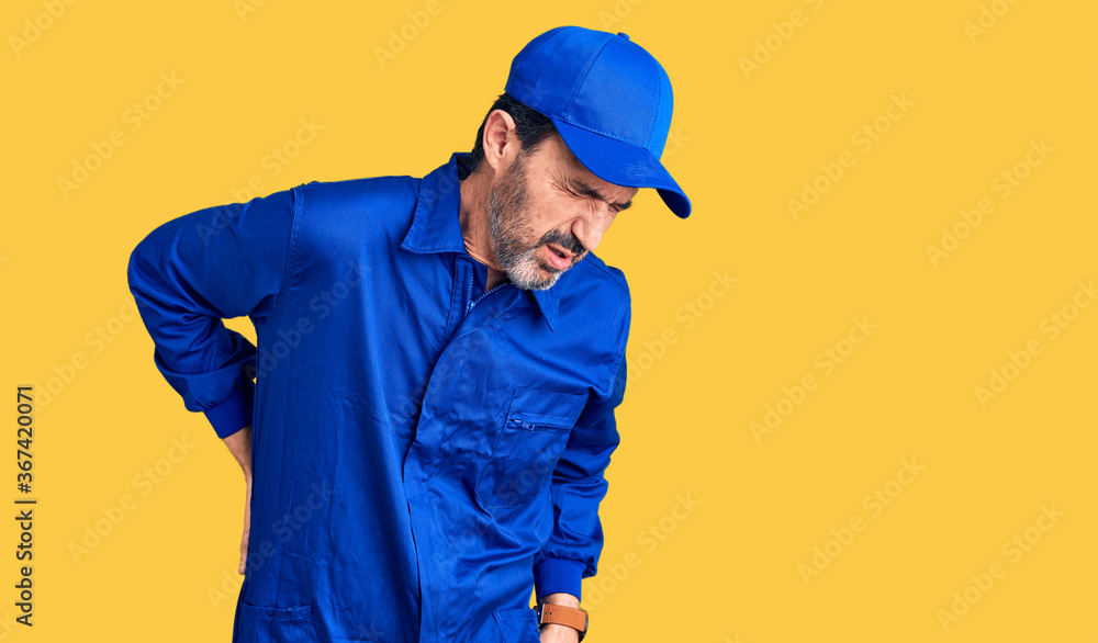 Middle age handsome man wearing mechanic uniform suffering of backache, touching back with hand, muscular pain