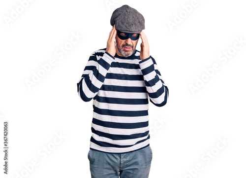 Middle age handsome man wearing burglar mask with hand on head for pain in head because stress. suffering migraine.