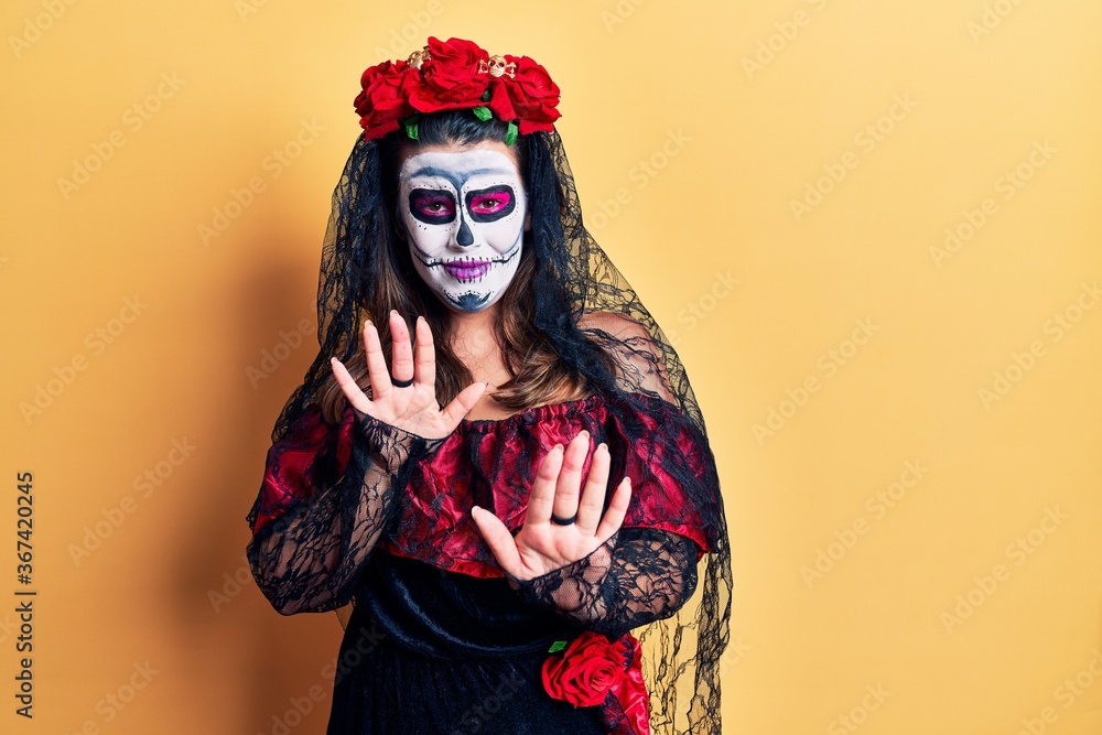 Young woman wearing day of the dead costume over yellow disgusted expression, displeased and fearful doing disgust face because aversion reaction. with hands raised Young woman wearing day of the dead costume over yellow disgusted expression, displeased and fearful doing disgust face because aversion reaction. with hands raised