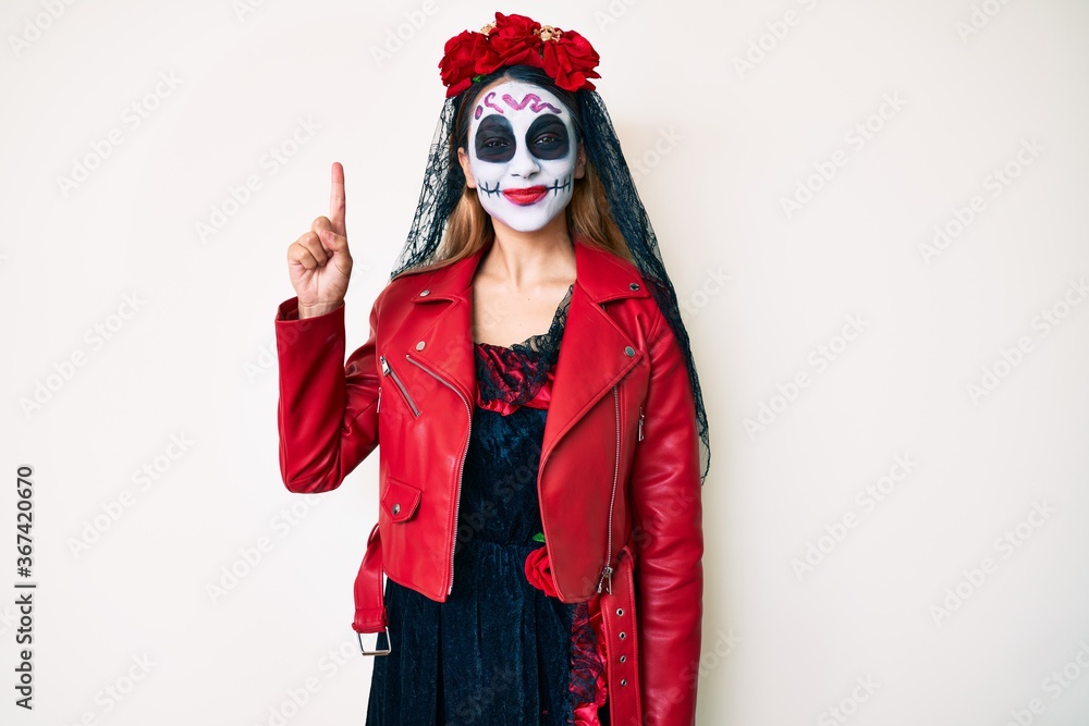 Woman wearing day of the dead costume over white showing and pointing up with finger number one while smiling confident and happy. Woman wearing day of the dead costume over white showing and pointing up with finger number one while smiling confident and happy.