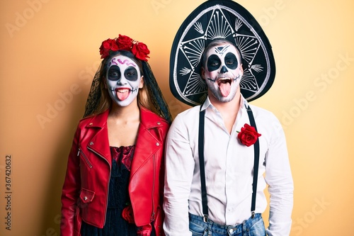 Couple wearing day of the dead costume over yellow sticking tongue out happy with funny expression. emotion concept.