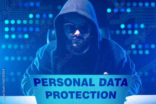 Violation of the law on personal data protection. A man in black clothing and glasses unlawfully receives personal data of people. The man behind the computer hides his face. Anonymity. photo