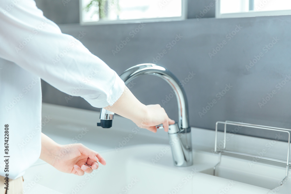 Fototapeta premium 爽やかな白いキッチンで女性が手を洗おうとしている