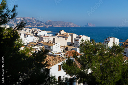 View over the white washed houses between fir trees with acient roofs to the ocean and the rock of Calpe, Altea, Costa Blanca, Spain
