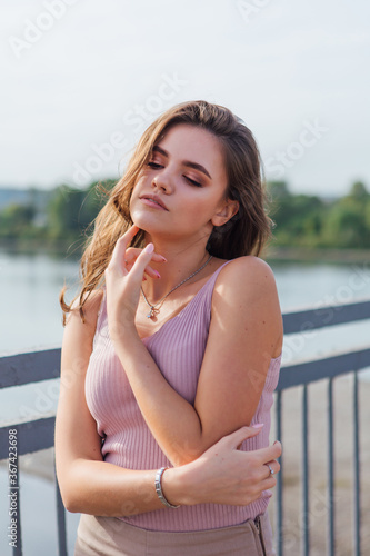 Pretty young woman posing on the old rusty transport bridge over the river during sunset.