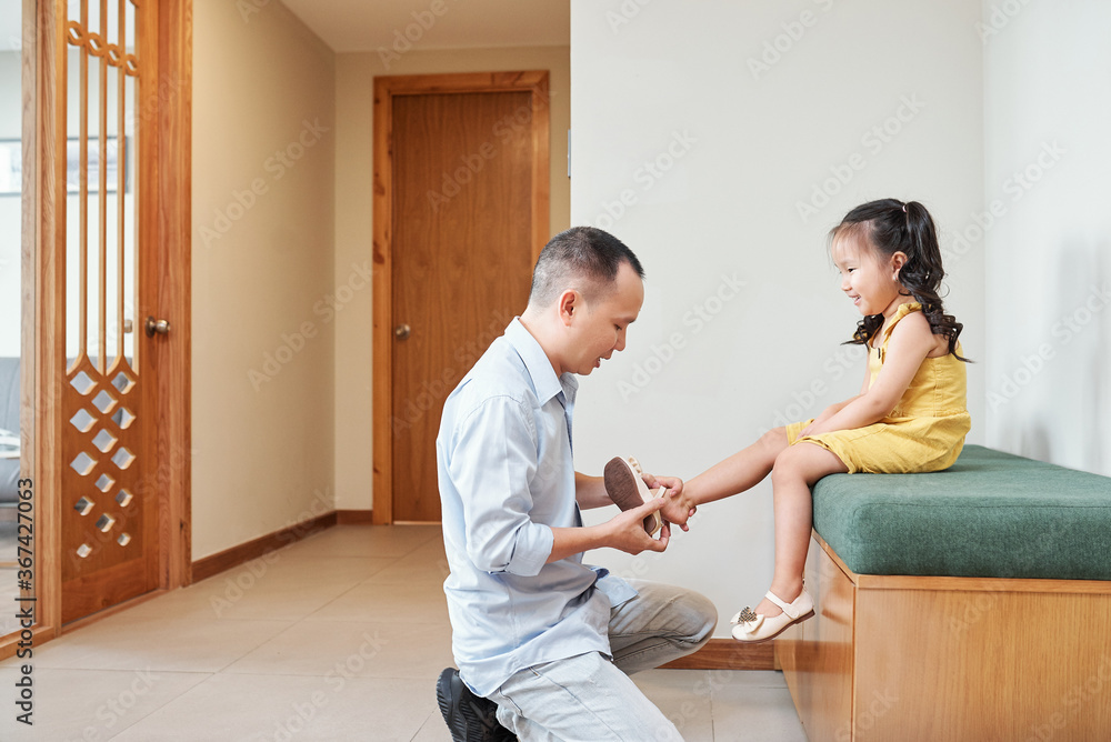 Happy pretty little Asian girl letting father to put on her shoes before they go for a walk Happy pretty little Asian girl letting father to put on her shoes before they go for a walk