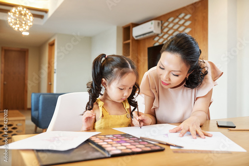 Pretty Asian woman helping daughter with painting when they are spending time at home due to quarantine