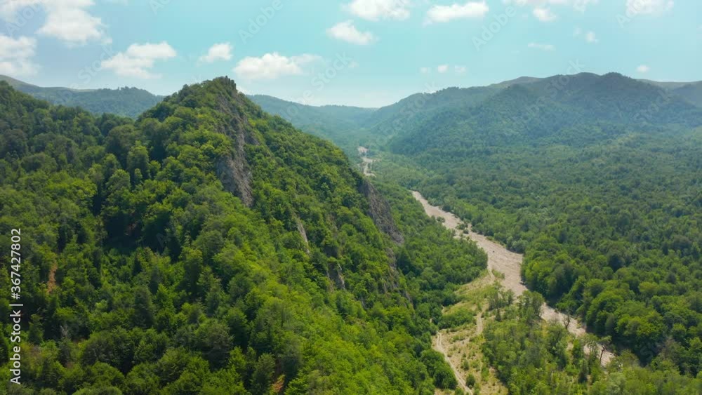 Aerial view of wild green forested mountains and cliffs in Kakheti region in Georgia. Beautiful blue sky with white sparse clouds. Backward movement, pan to left. 4k footage. Aerial view of wild green forested mountains and cliffs in Kakheti region in Georgia. Beautiful blue sky with white sparse clouds. Backward movement, pan to left. 4k footage.