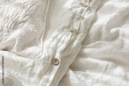 Trendy organic natural linen bedclothes with wooden buttons closeup. Bedding, morning light, bedroom style and design. Rough textile background with wrinkle.