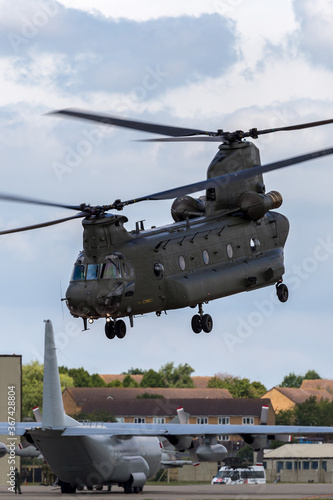 Large twin rotor military helicopter taking off from a military airbase.