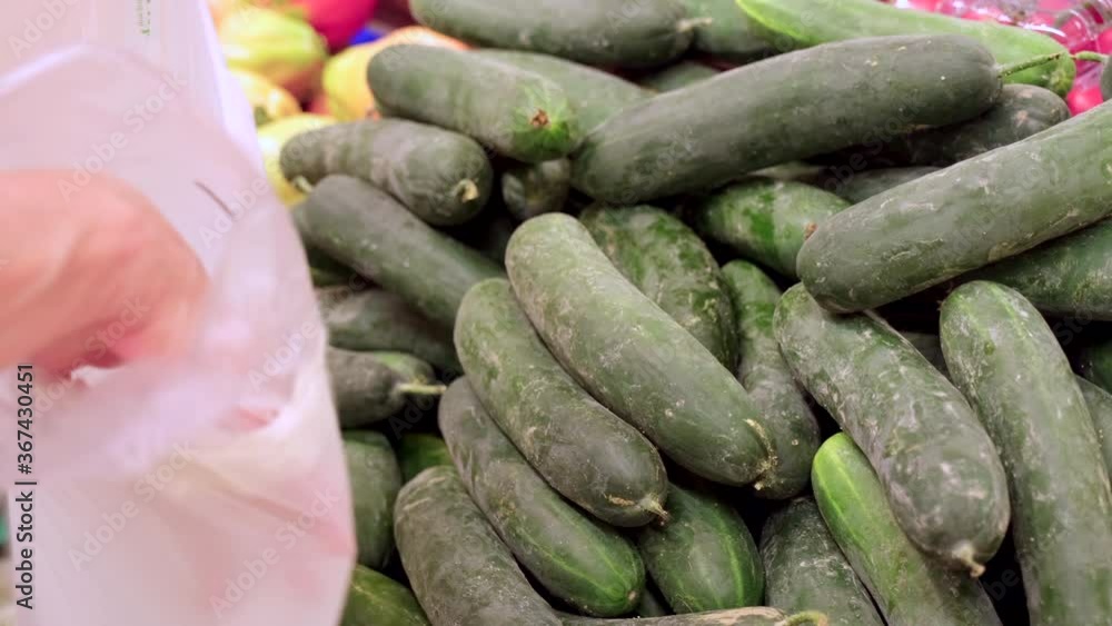 Picking cucumber at the vegetables market. Hand choosing healthy vegetarian food in grocery store at slow motion.