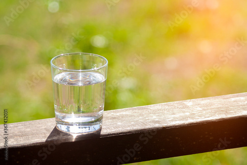 Water glass stands on wooden plank on sunbeams. Hydration at hot summer days concept. Healthy lifestyle symbol. Healthy water drink sunny