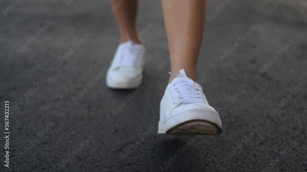 Closeup of woman's white sneakers walking towards camera on cracked asphalt Closeup of woman's white sneakers walking towards camera on cracked asphalt