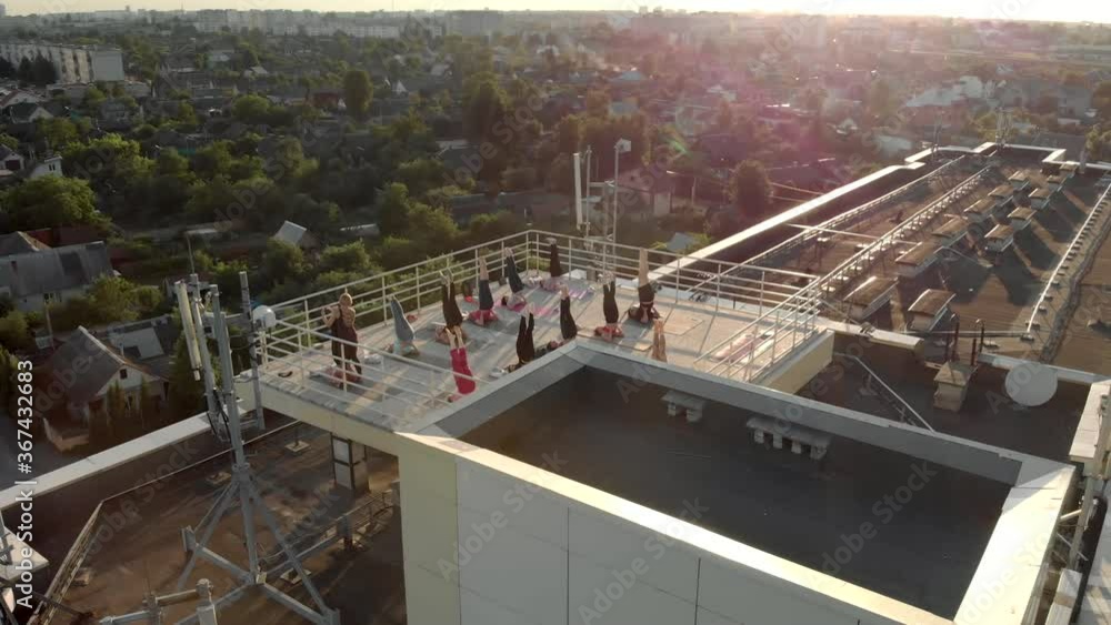 A group of healthy, happy people practicing on the mats in the open air on the roof. Women with an instructor perform Sarvangasana standing on their shoulder blades
