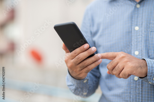 Close up male hands holding using black smartphone on city background.